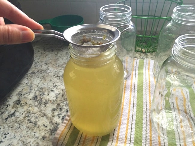 Pouring homemade chicken broth into jars for canning.