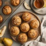Pear muffins cooling on a wire rack with sliced pears in the background