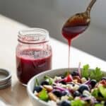 Homemade blueberry vinaigrette in a glass jar beside a fresh green salad with blueberries and goat cheese