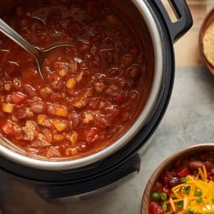 Bowl of award-winning Instant Pot chili topped with shredded cheese, jalapeños, and fresh herbs on a rustic wood table.