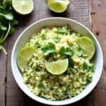 Serving spoon scooping cilantro lime rice from a bowl with lime slices on the side