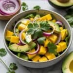 Close-up of colorful mango avocado salad with lime wedges and fresh herbs