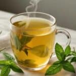 A steaming cup of lemon balm tea with fresh lemon balm leaves on the side