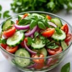 Cucumber tomato salad topped with crumbled feta cheese and fresh basil