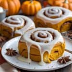 Soft pumpkin cinnamon rolls topped with cream cheese icing on a fall table