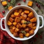 Golden roasted butternut squash cubes on a white holiday serving dish with herbs.