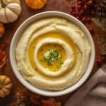 Bowl of creamy mashed potatoes topped with butter and herbs