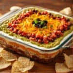 Holiday 7-layer dip topped with red tomatoes, green onions, and black olives in a festive dish
