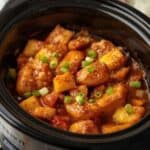 A white bowl filled with slow cooker sweet and sour chicken, vibrant bell peppers, and pineapple chunks over fluffy white rice.