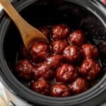 Close up of a meatball on a toothpick with a glossy red grape jelly and chili sauce glaze.