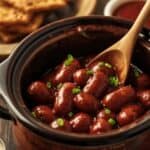 Someone pouring BBQ sauce and grape jelly over cocktail sausages in a slow cooker.