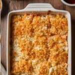 A top-down view of a creamy salmon sushi bake in a white baking dish topped with green onions and a drizzle of spicy mayo.