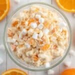 A close-up shot of a silver spoonful of creamy orange fluff salad featuring mandarin oranges and whipped cream.